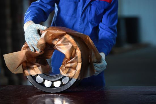 The worker manually packs the finished bearing. Bearing production concept. Photo in the interior of the plant. Portrait of a man in overalls.